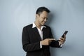 A portrait of a happy Asian businessman is smiling and holding his smartphone wearing black suit isolated by a blue background Royalty Free Stock Photo