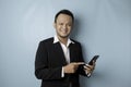 A portrait of a happy Asian businessman is smiling and holding his smartphone wearing black suit isolated by a blue background Royalty Free Stock Photo