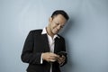 A portrait of a happy Asian businessman is smiling and holding his smartphone wearing black suit isolated by a blue background Royalty Free Stock Photo