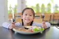 Portrait of happy Asian child girl eating Pork steak and vegetable salad on the table with holding knife and fork. Children having Royalty Free Stock Photo