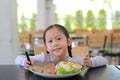 Portrait of happy Asian child girl eating Pork steak and vegetable salad on the table with holding knife and fork. Children having Royalty Free Stock Photo