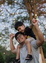 Portrait of happy Asian father giving son piggyback ride on his shoulders and looking up Royalty Free Stock Photo