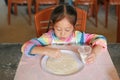 Portrait of happy asian little girl kneading pizza dough on table. Homemade process of preparation pizza