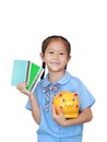 Portrait of happy Asian little girl in school uniform holding account book and piggy bank isolated over white background. Royalty Free Stock Photo