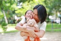 Portrait of happy Asian mother cuddle daughter and hugging teddy bear doll in the garden. Mom and child girl with love and Royalty Free Stock Photo