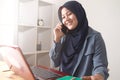 Happy Asian muslim businesswoman female entrepreneur making business phone call while working at home