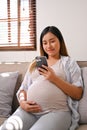 Portrait of a happy Asian pregnant woman using her phone while relaxing on sofa in living room Royalty Free Stock Photo