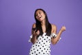 Portrait of a happy asian woman in dress standing isolated over violet background, using moible phone Royalty Free Stock Photo