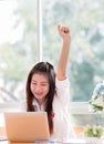 Portrait of happy Asian woman manager sitting at her laptop computer in work office and raised hands up with smiling because Royalty Free Stock Photo