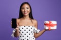 Portrait of a happy asian woman standing isolated over violet background, holding present box,