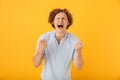 Portrait of happy astonished man 20s screaming and clenching fists with closed eyes, isolated over yellow background