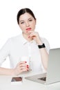 Portrait of happy attractive brunette businesswoman in white shirt sitting, holding cup of drink, touching her chin and looking at Royalty Free Stock Photo