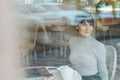 Portrait of happy attractive smiling woman with shor hair wearing sitting in cafe looking through a window, view through