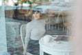 Portrait of happy attractive smiling woman with shor hair wearing sitting in cafe looking through a window, view through