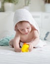 Portrait of happy baby in hooded towel playing with yellow rubber duck on bed after bathing Royalty Free Stock Photo