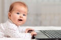 Portrait of happy baby is lying on the bed and holding on to the laptop with his hands. Copy space. The concept of entertainment Royalty Free Stock Photo