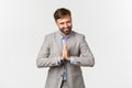 Portrait of happy bearded businessman in grey suit, thanking for something, holding hands pressed together and bowing