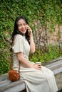 A happy Asian woman is on the phone with her friend while sitting on a bench in the city Royalty Free Stock Photo