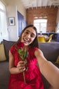 Portrait of happy beautiful biracial woman holding rose bouquet during virtual date at home