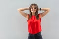 Portrait of happy beautiful brunette young woman in red shirt standing, holding her head and looking at camera with toothy smile Royalty Free Stock Photo