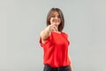 Portrait of happy beautiful brunette young woman in red shirt standing, pointing and looking at camera with toothy smile and Royalty Free Stock Photo