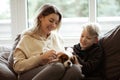 Portrait of happy beautiful middle-aged woman sitting on grey sofa with teenage boy at home, holding dog, stroking pet. Royalty Free Stock Photo