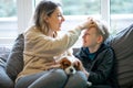 Portrait of happy beautiful middle-aged woman sitting on sofa with teenage boy at home, holding dog, patting sons head. Royalty Free Stock Photo