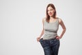 portrait of happy beautiful slim waist of young woman in big jeans and gray top showing successful weight loss Royalty Free Stock Photo