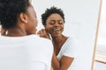 Portrait of happy beautiful young African American woman in white t-shirt puts on earring near mirror Royalty Free Stock Photo