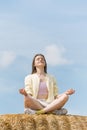 Portrait of happy beautiful young woman meditating sitting in the hay against blue sky. Unity with nature Royalty Free Stock Photo