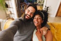 Portrait of happy biracial bearded man holding girlfriend's hands and taking selfie on sofa Royalty Free Stock Photo