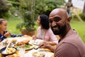 Portrait of happy biracial father at table having meal with wife and daughter in garden Royalty Free Stock Photo