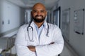 Portrait of happy biracial male doctor wearing lab coat and stethoscope in corridor at hospital Royalty Free Stock Photo