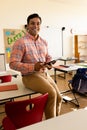 Portrait of happy biracial male teacher with tablet in elementary school classroom Royalty Free Stock Photo