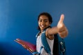 Portrait of happy biracial schoolgirl making thumbs up sign holding notebooks with copy space