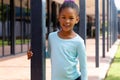 Portrait of happy biracial schoolgirl smiling, holding post in sunny schoolyard