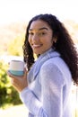 Portrait of happy biracial woman holding cup of coffee in sunny nature Royalty Free Stock Photo