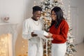 Portrait of happy black couple holding gift and standing near Christmas tree Royalty Free Stock Photo