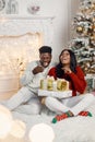 Portrait of happy black couple holding gifts and sitting near Christmas tree Royalty Free Stock Photo