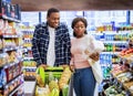 Portrait of happy black couple with shopping cart full of products choosing food together at modern supermarket Royalty Free Stock Photo