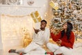 Portrait of happy black couple throwing gifts in the air while sitting near Christmas tree Royalty Free Stock Photo