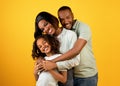 Portrait of happy black family of three with cute daughter embracing and smiling to camera over yellow background Royalty Free Stock Photo