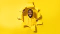 Portrait of happy black man standing in torn paper hole, looking and smiling at camera through yellow background Royalty Free Stock Photo