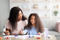 Portrait of happy black mother and her daughter painting with watercolors and gouache at home. Family hobbies concept