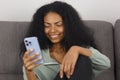 Portrait of happy black woman browing smart phone app. Cheerful BIPOC female using new mobile phone on couch at home