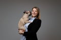 Portrait of a happy blonde woman breeder holds her cute pug. on gray background.