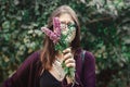 Portrait of happy boho girl in sunglasses smiling with bouquet of wildflowers in sunny garden. Stylish hipster carefree girl