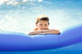 Portrait of a happy boy in a blue pool. A happy child swims in an inflatable pool in the garden on a sunny summer day Royalty Free Stock Photo