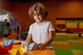 Portrait of happy boy child making origami paper toys at indoor playroom