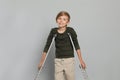 Portrait of happy boy with crutches on grey background Royalty Free Stock Photo